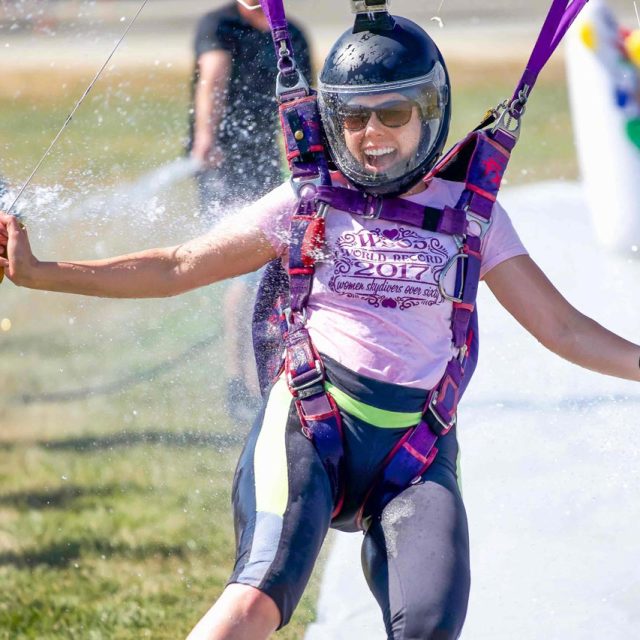 Female professional skydiver sliding through water on feet while landing parachute