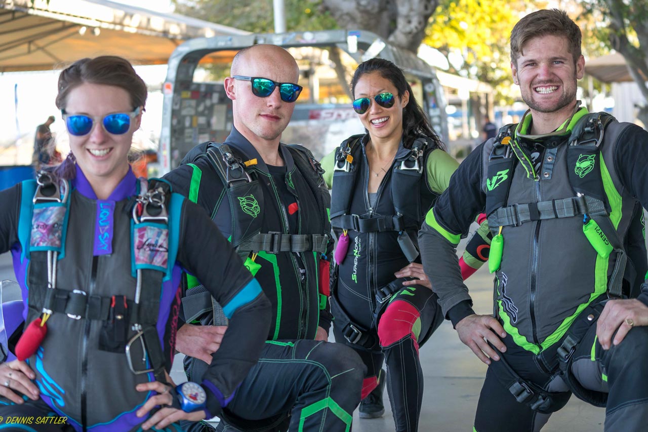 Two men and two women kneel in jumpsuits and full skydiving gear