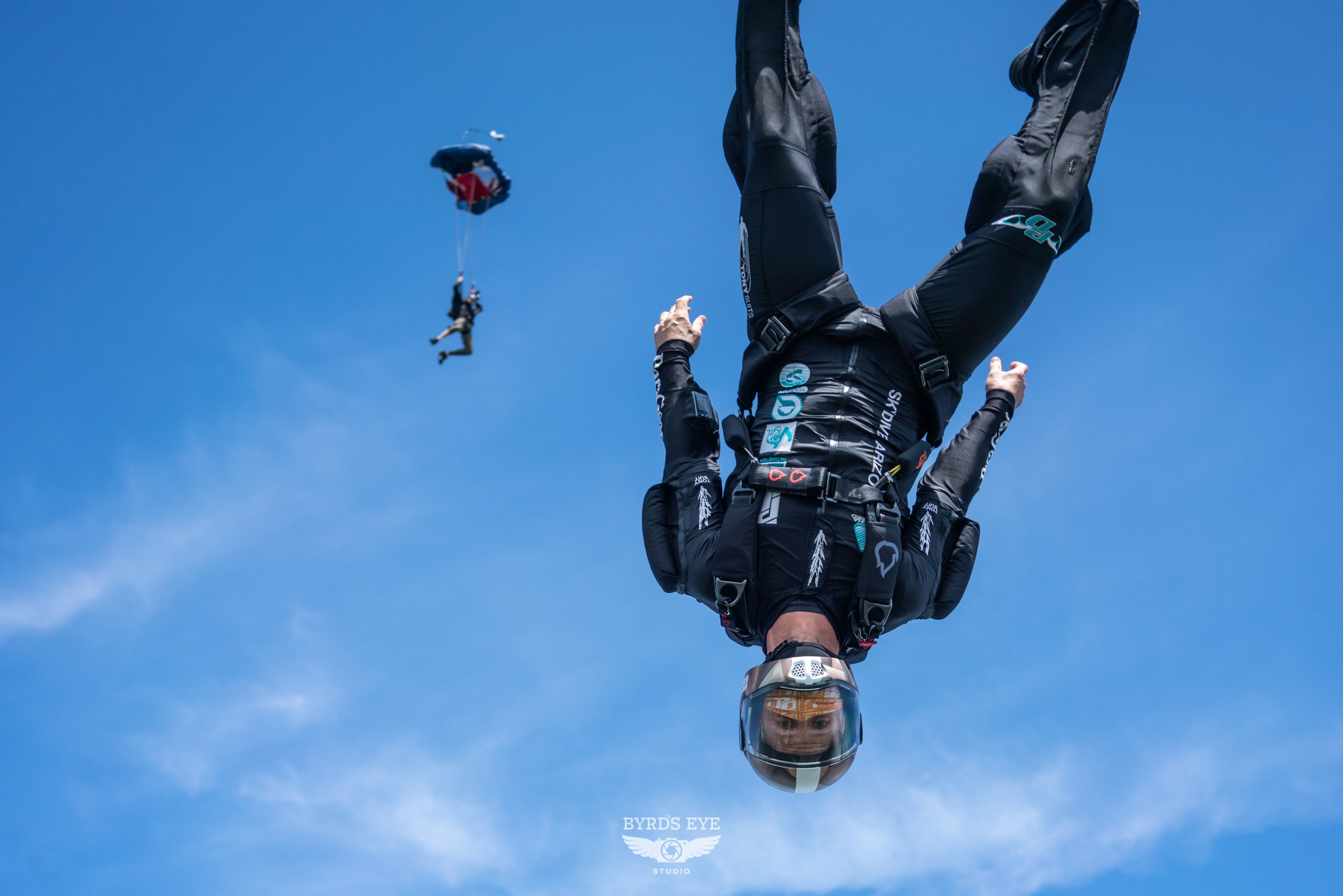 Experienced skydiver wearing black jumpsuit flying head down in freefall