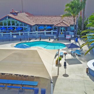 Concrete surrounds a light blue pool in front of a blue building with terra cotta tiles on the roof