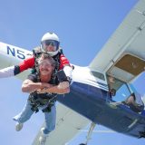 Male tandem skydiving student and instructor smiling for camera after exiting aircraft