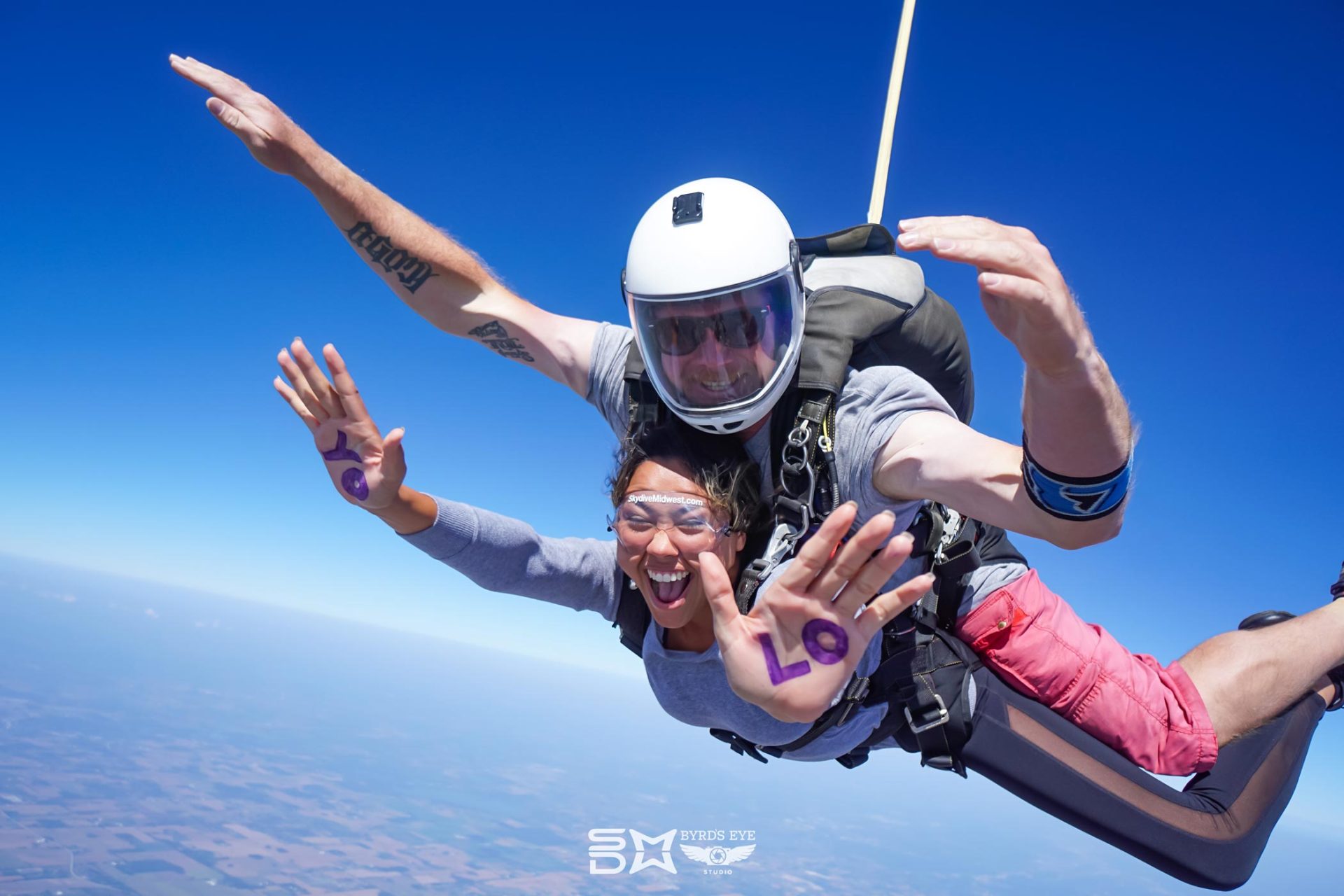 Female tandem skydiving student in freefall with YOLO written on her palms