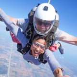 Female tandem skydiving student in freefall smiling at the camera