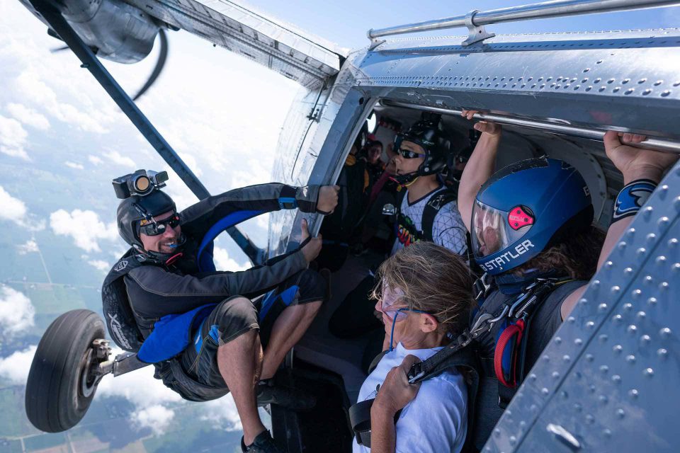 Videographer holding on to the frame of an airplane door capturing a tandem student and instructor preparing to exit