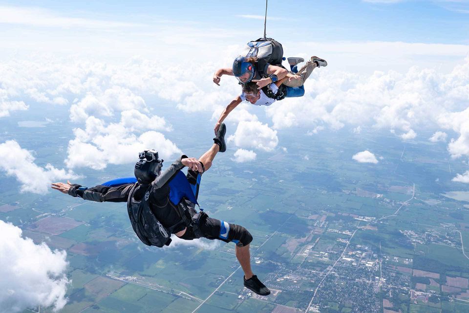 Outside view of a tandem skydiving student and instructor in freefall holding on to the foot of a videographer