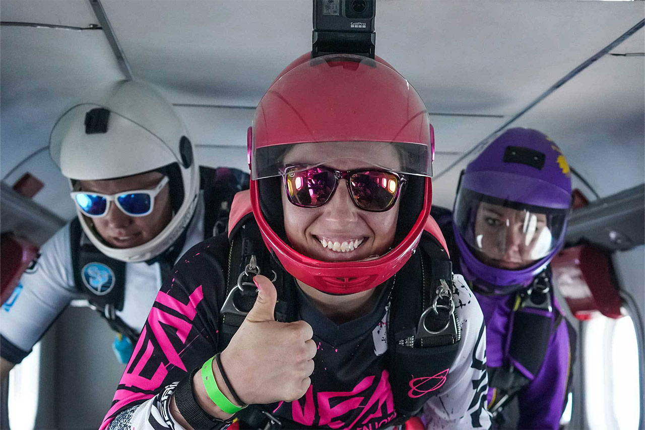 Licensed skydiver with colorful helmet and jumpsuit smiling for camera in an airplane