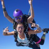 Female tandem skydiving student and instructor in freefall giving rock on sign with hands