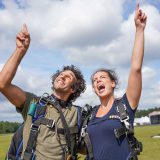 Tandem skydiving student and instructor on ground pointing up at sky